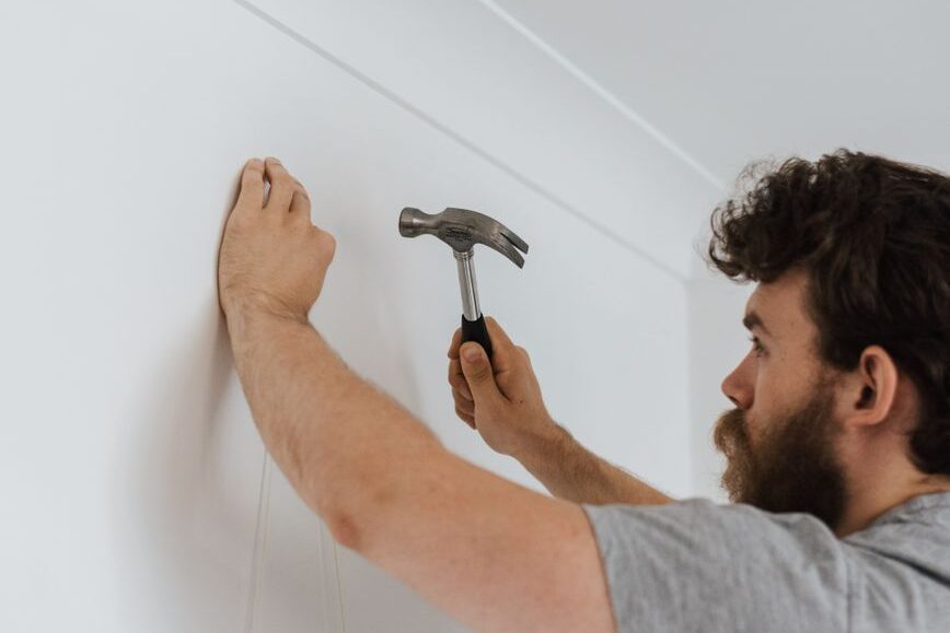 man hammering nail into wall during housework | GenadePro
